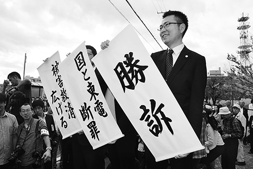 ▶勝訴の旗を掲げる原告側の弁護士、福島地裁前。